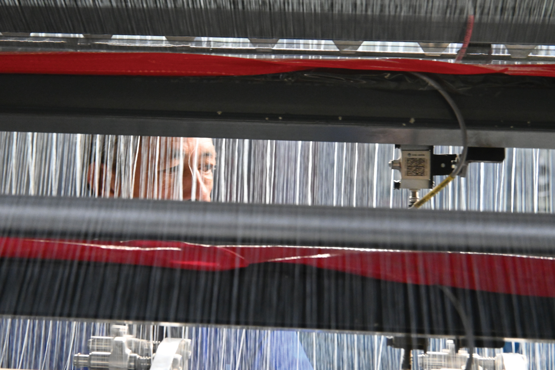 Operator viewed through warp threads on a Jacquard loom with red and black yarn