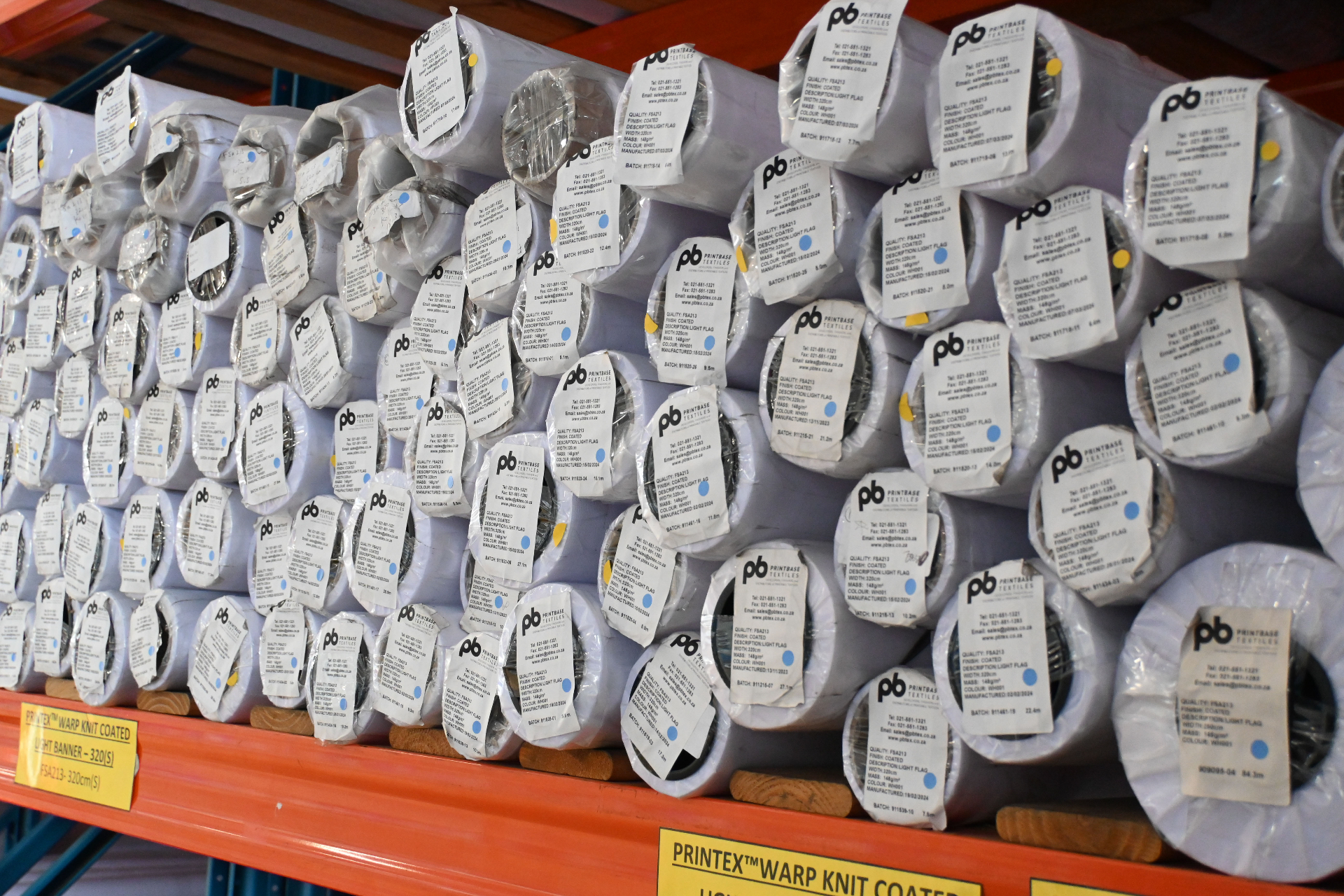 Pallet rack stacked with rolls of Printex warp-knit coated light banner labelled FSA213