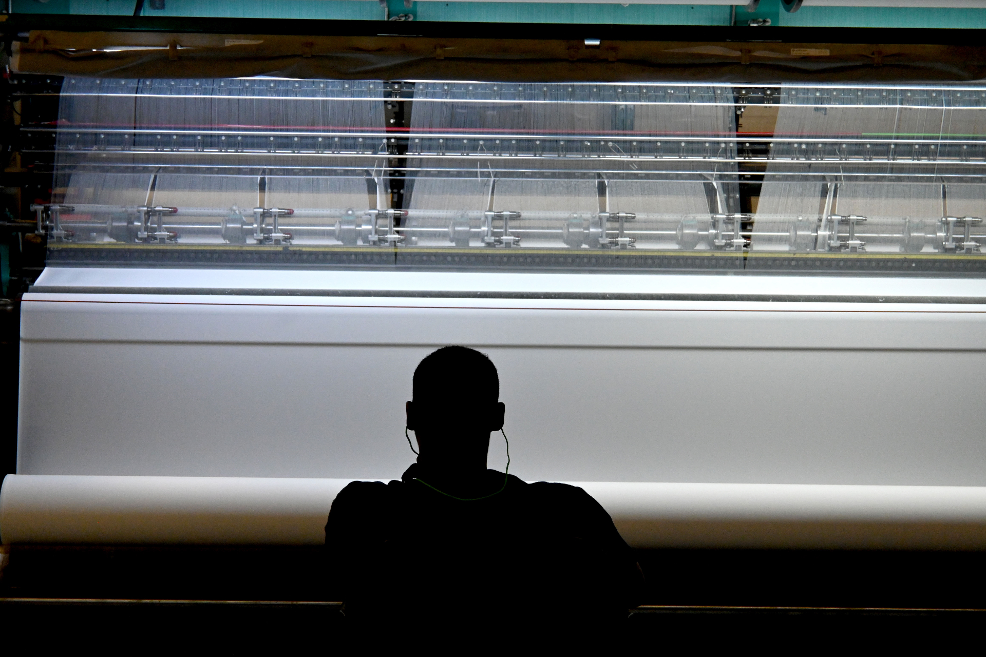 Silhouette of operator at a Karl Mayer warp-knit machine producing white fabric