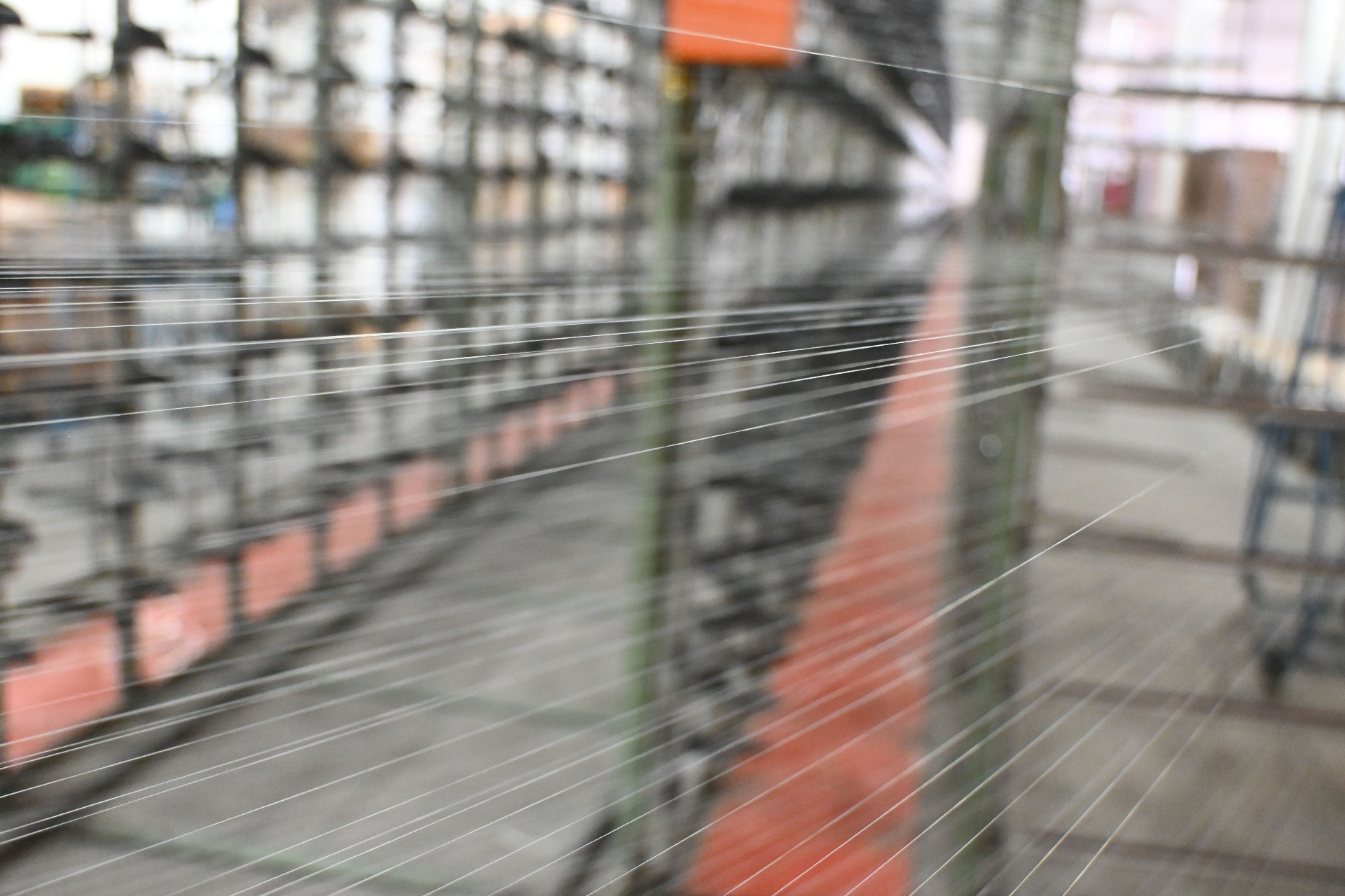 Warp threads stretched across the creel toward the knitting machine in shallow focus