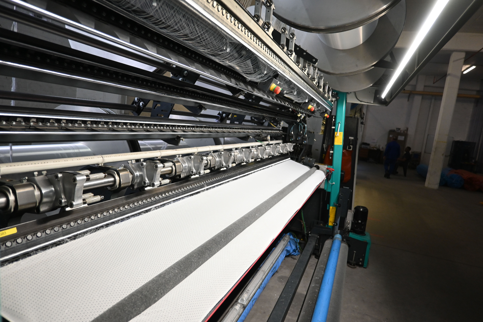 Close-up of the warp-knitting machine bed producing white textile