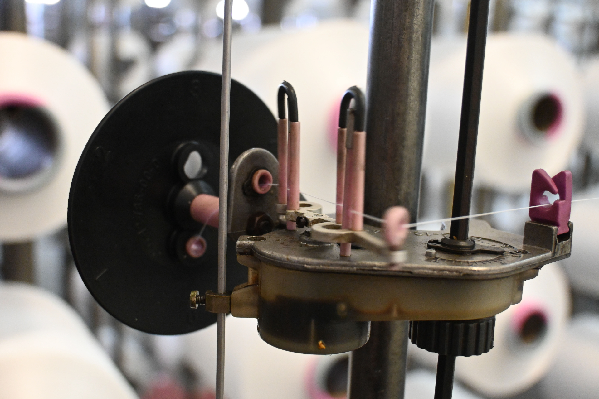 Macro view of yarn tensioner with pink ceramic guides on twisting machine