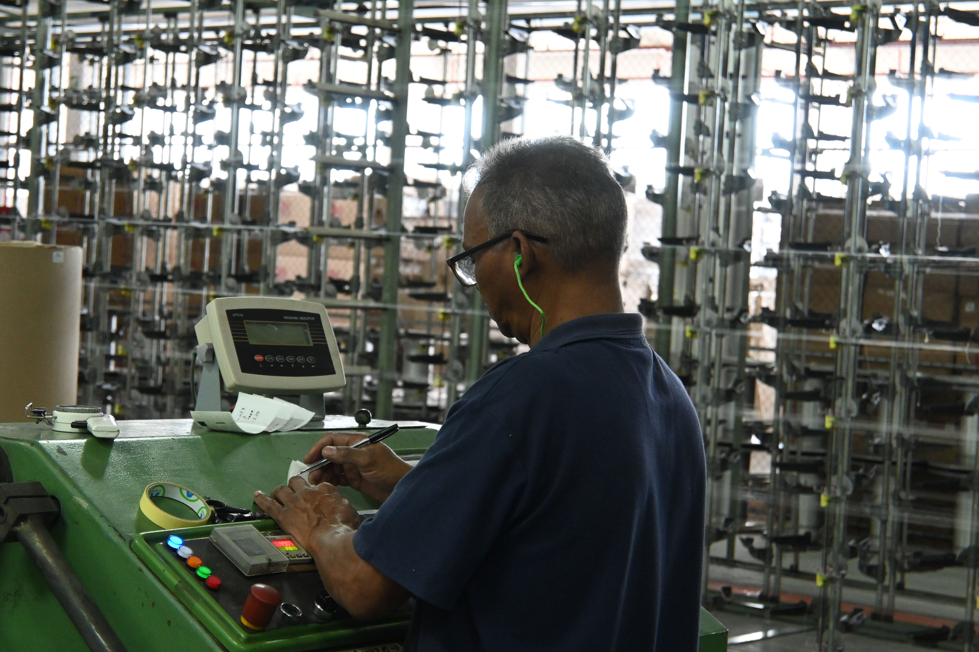 Operator at a weighing indicator station in front of a large creel rack
